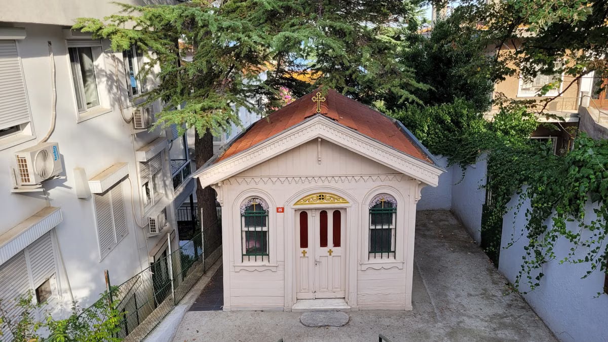 A quaint chapel nestled between buildings, surrounded by greenery.